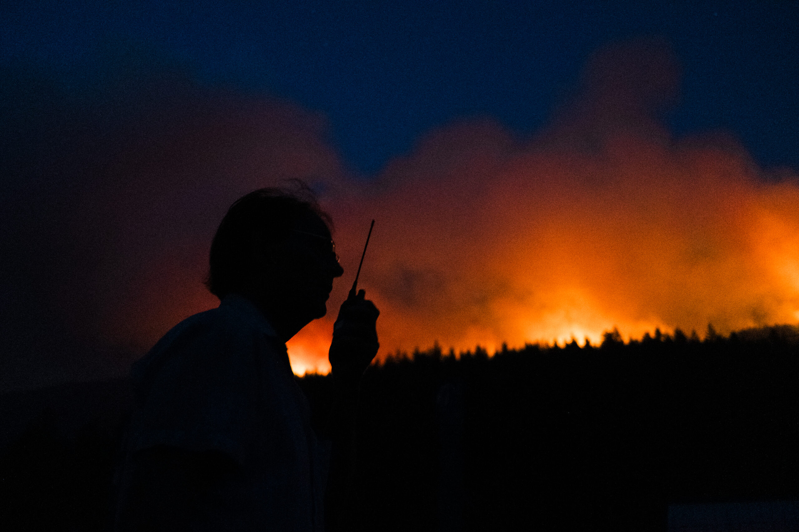 the silhouette of a volunteer firefighter in Argenta is framed by glowing red flames