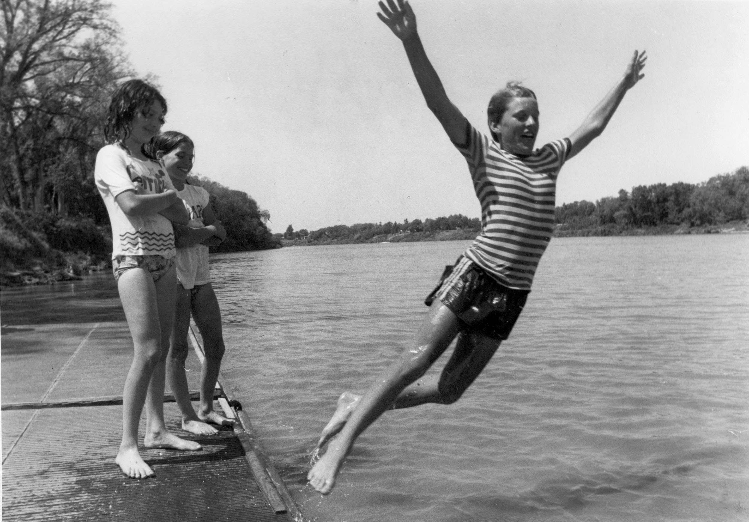 black and white photo of young people jumping into a river